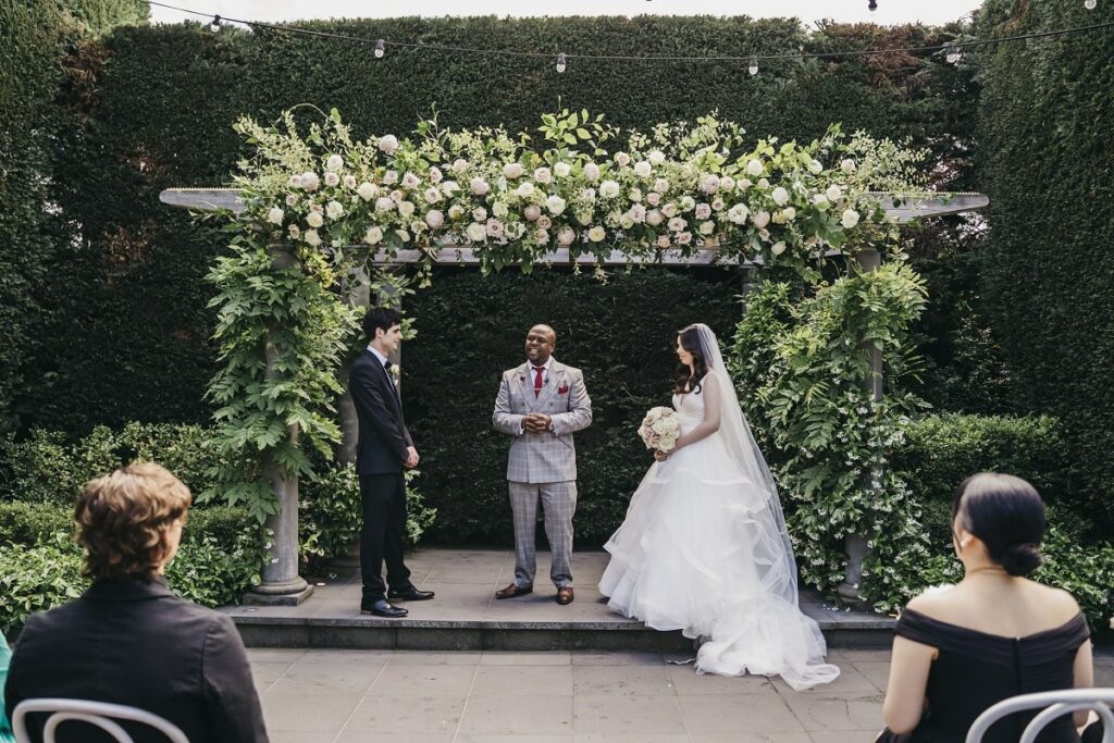 Sophia and Kyle, with their wedding officiant, standing next to a rose-filled ceremony arch