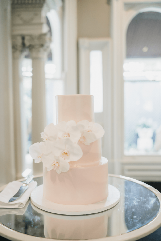 Three-tier wedding cake with blush buttercream adorned with a stem of orchids